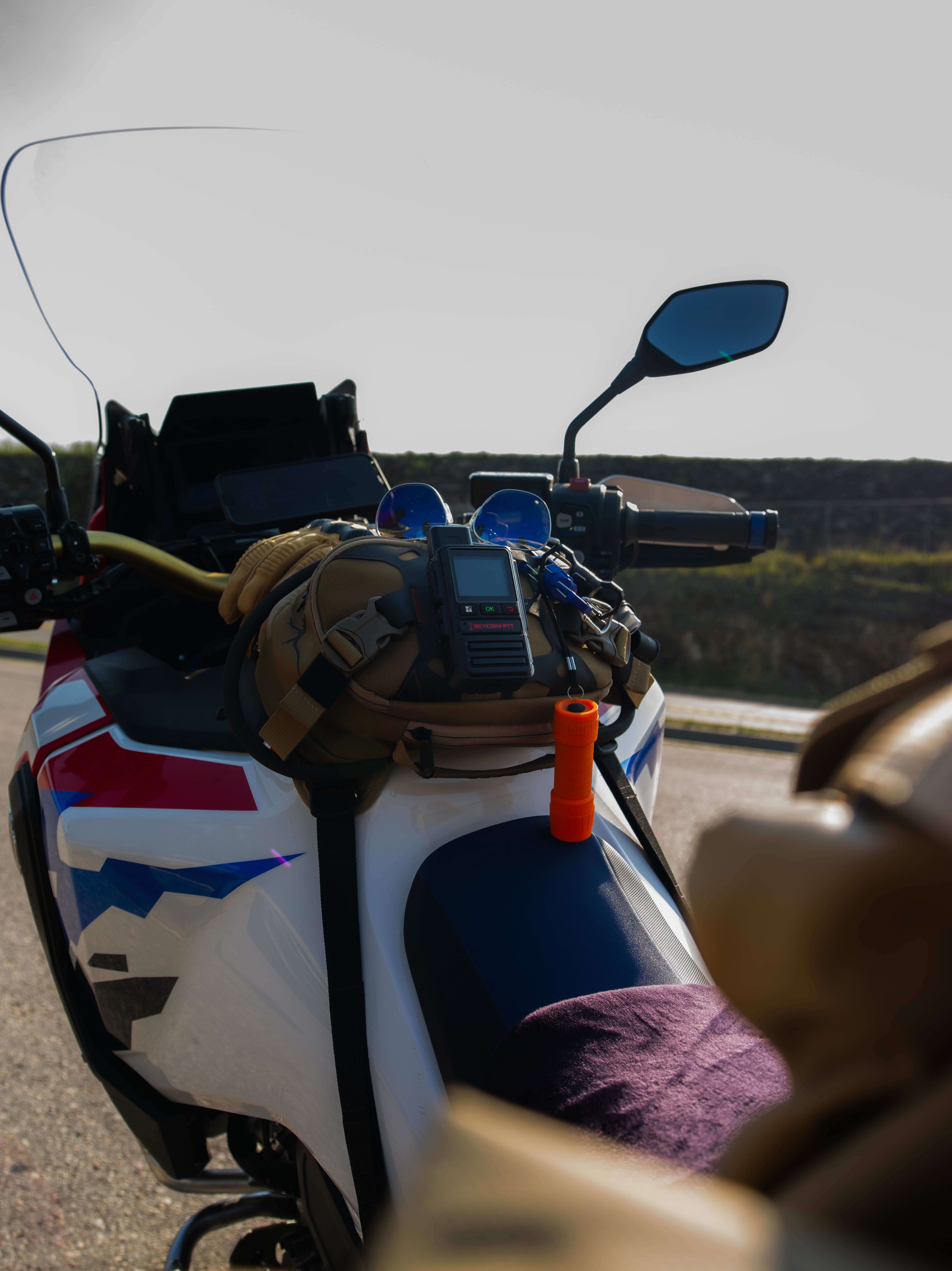 SkyCom PTT radio mounted on a motorcycle tank bag on the road