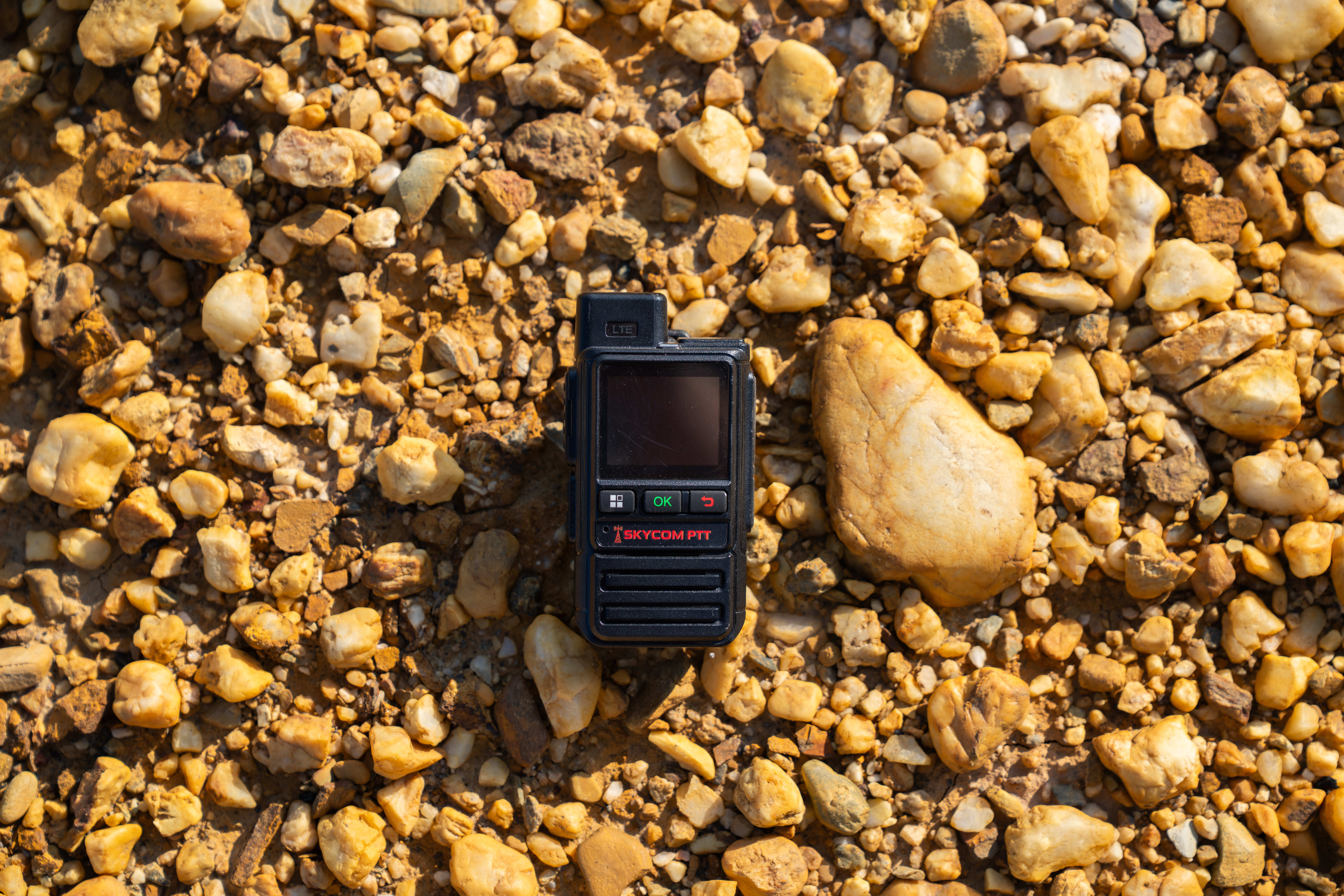 SkyCom PTT radio resting on sunlit river rock